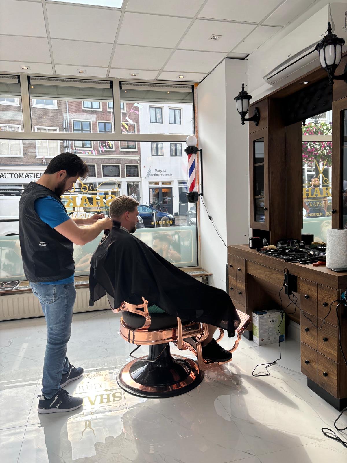 De barbier knipt een klant bij het grote voorraam, buiten de Waterstraat